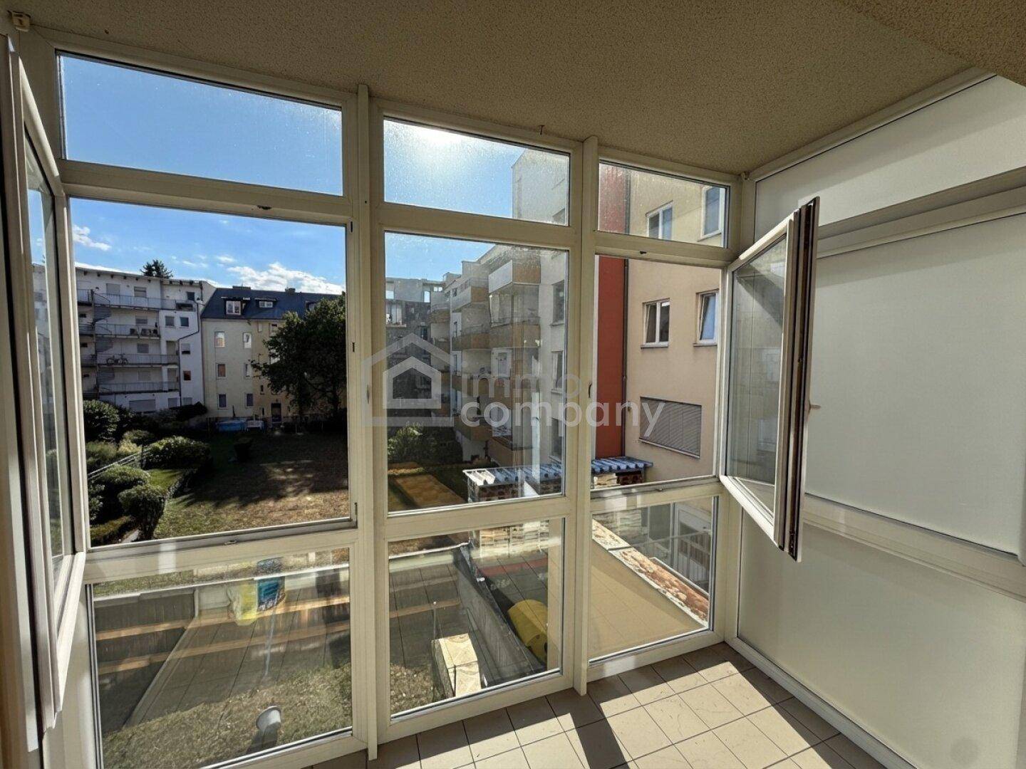 Verglaste Loggia mit Blick auf den Innenhof und umliegende Wohngebäude.