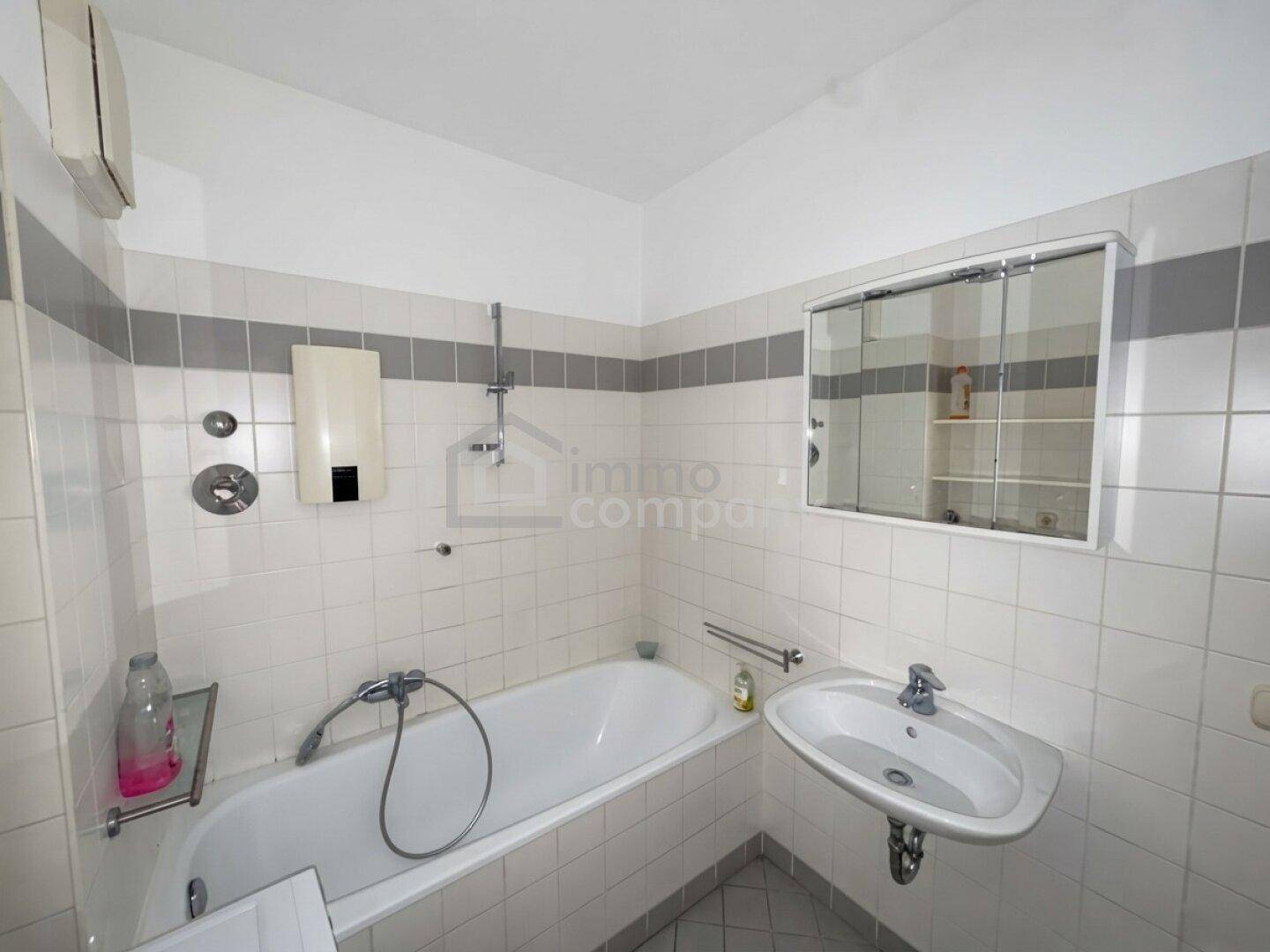 Gefliestes Badezimmer mit Badewanne, Duschfunktion, Waschbecken und Spiegelschrank.