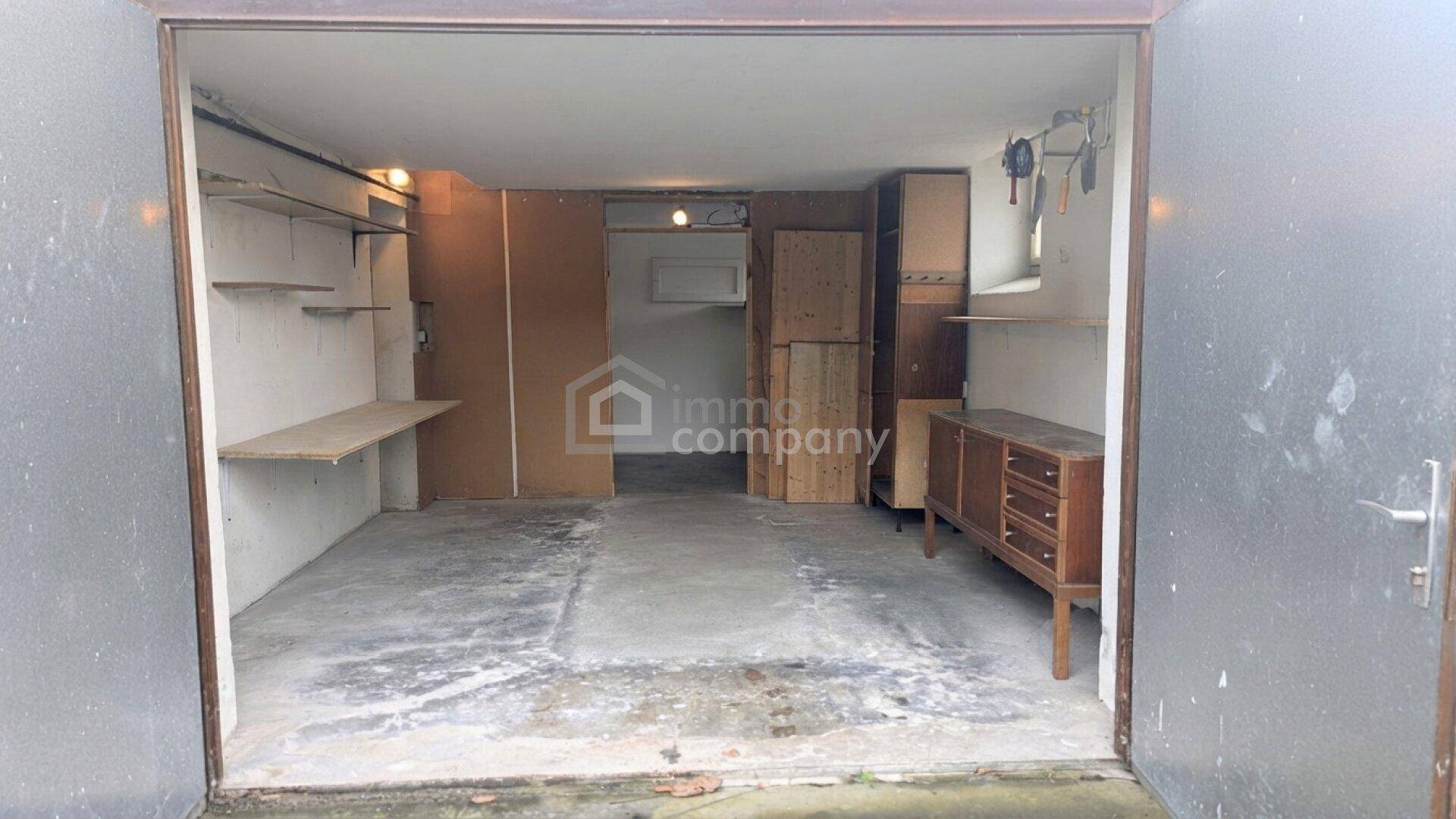 Geräumige Garage mit Betonboden und zusätzlichen Abstellmöglichkeiten für diverse Gegenstände.