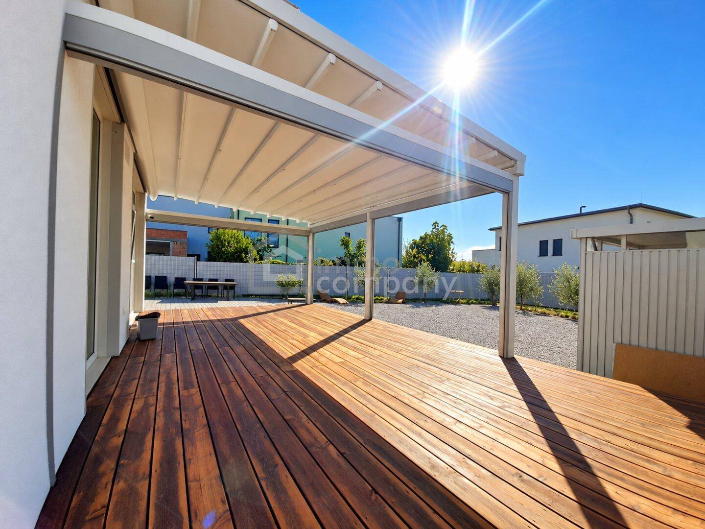 Sonnige Holzterrasse mit ausfahrbarer Pergola und Blick auf den Garten.