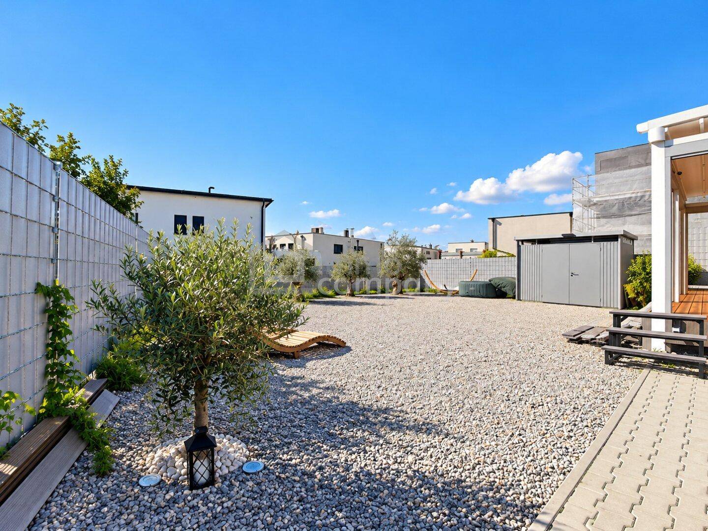 Weitläufiger Kiesgarten mit Gartenhaus und jungen Olivenbäumen.