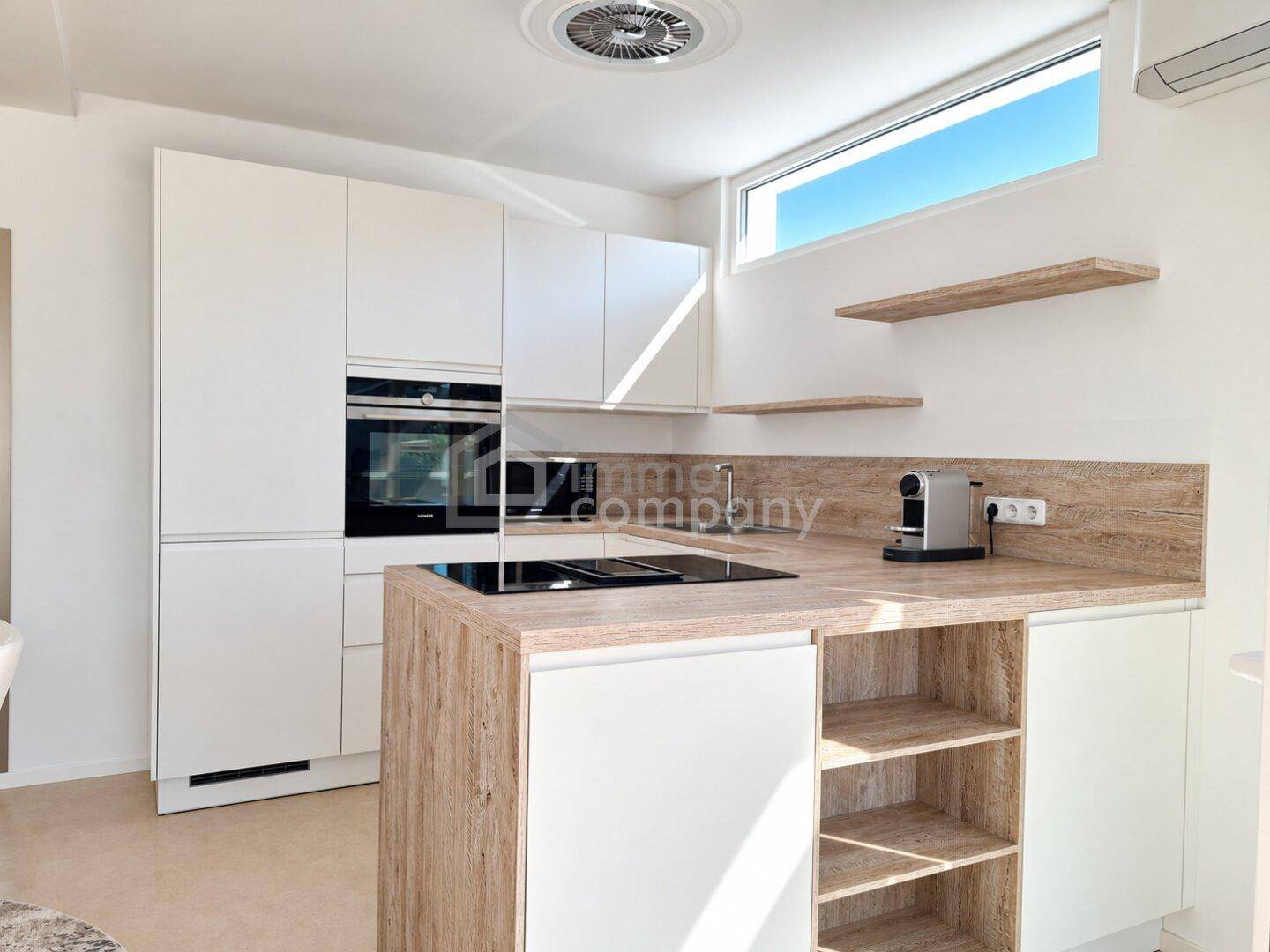 Moderne Einbauküche mit weißen Schränken, Holzdetails und Induktionskochfeld.