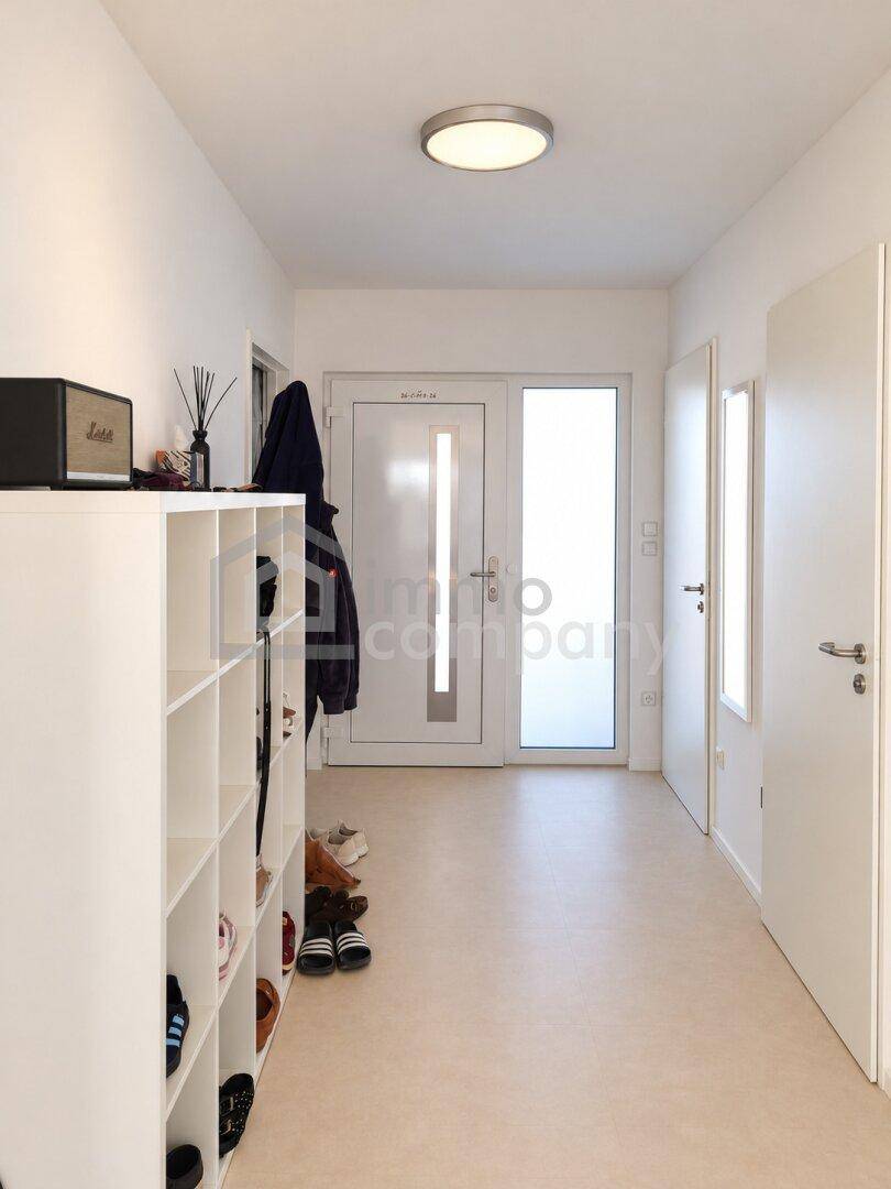 Heller Eingangsbereich mit Schuhregal und moderner Haustür.