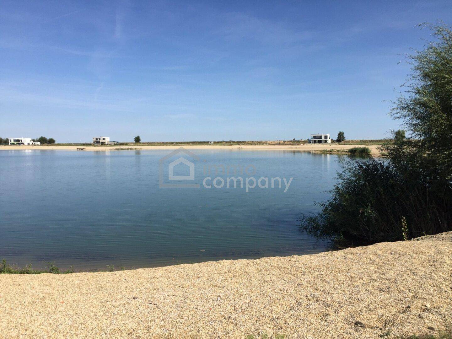 Weitläufiger Blick auf einen See mit Sandstrand und umliegenden Häusern.