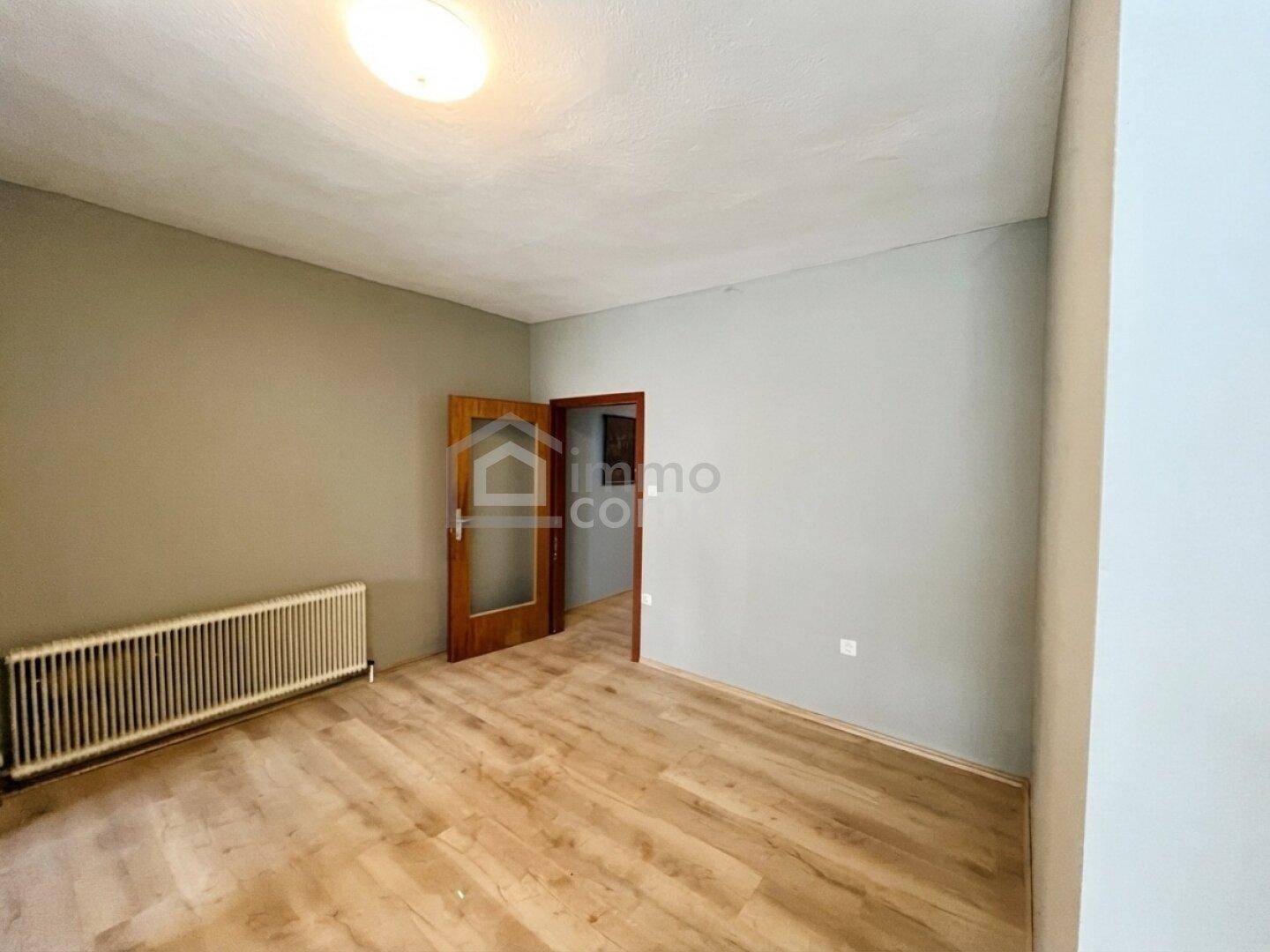 Leerer Raum mit hellgrauen Wänden, Laminatboden und zwei Holztüren, bereit zur individuellen Gestaltung.