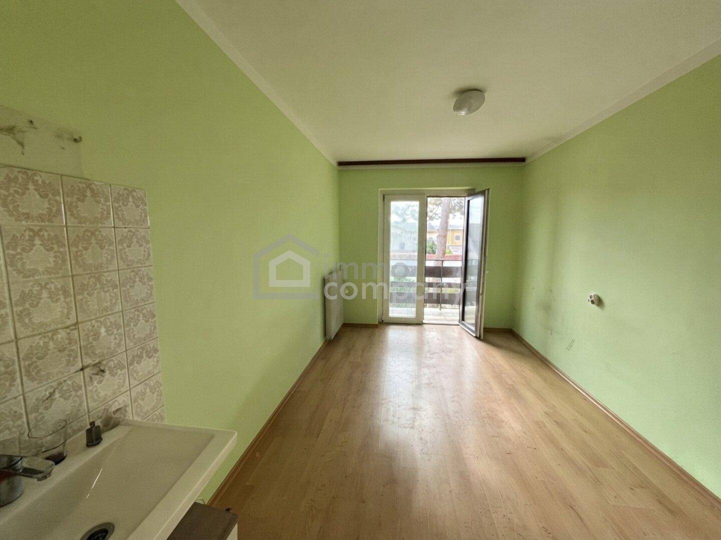 Leerer Raum mit hellgrünen Wänden, Laminatboden und Zugang zu einem kleinen Balkon.