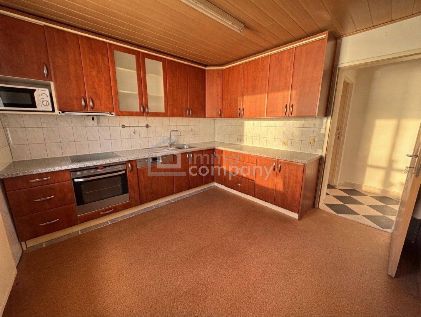 Küche mit Holzschränken, Fliesenboden und Blick in den angrenzenden Raum.