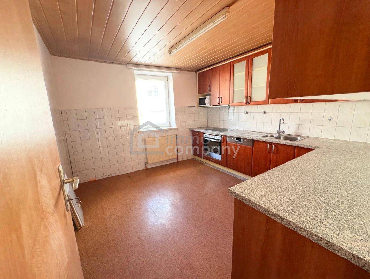 Helle Küche mit Holzschränken, Fliesenboden und einem Fenster für Tageslicht.