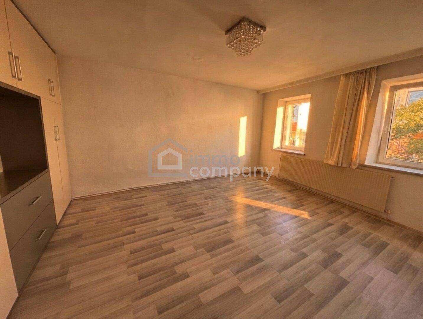Schlafzimmer mit Holzoptikboden, Einbauschrank und Fenstern für natürliches Licht.