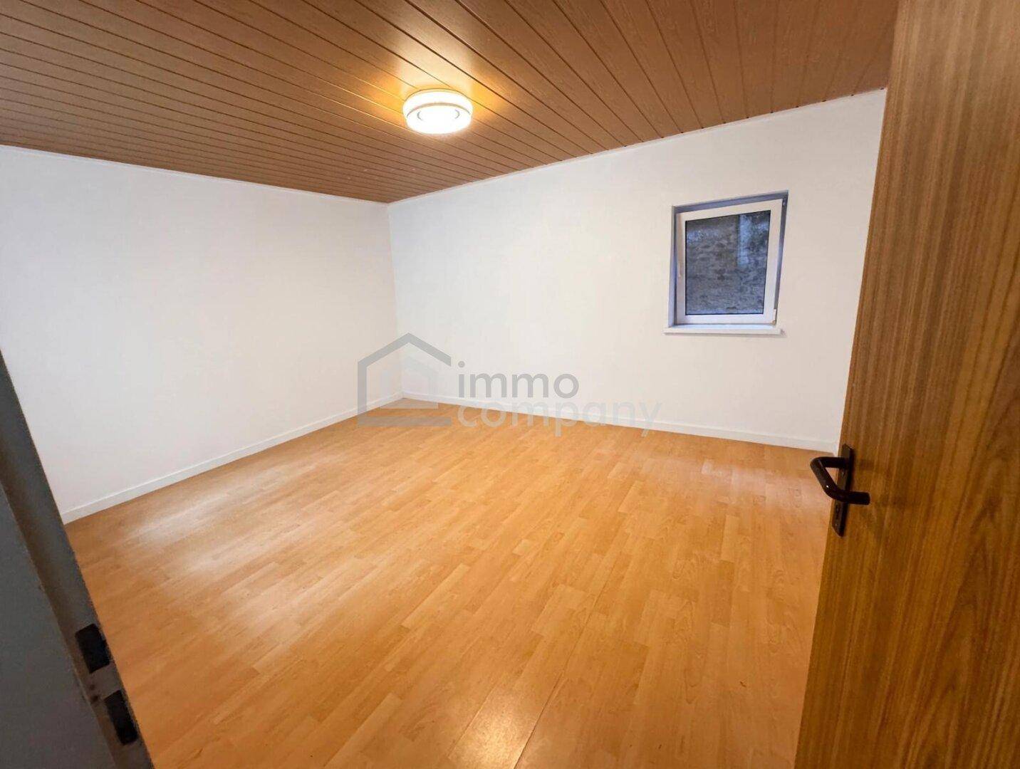 Leerer Raum mit Holzoptikboden und einem kleinen Fenster, ideal als Gästezimmer oder Büro.