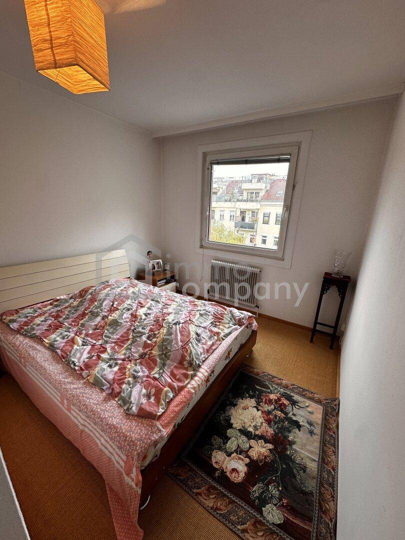 Schlafzimmer mit Teppichboden, Doppelbett und Blick auf die umliegenden Gebäude der Stadt.