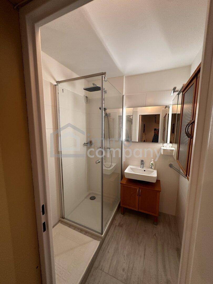 Modernes Badezimmer mit Duschkabine, Einzelwaschbecken und Holzoptik-Boden, hell und funktional.