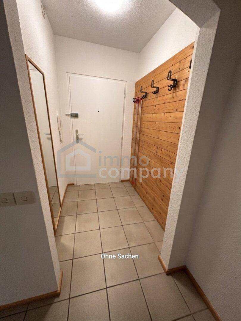 Heller Eingangsbereich mit Fliesenboden und Holzgarderobe, unmöbliert und aufgeräumt.