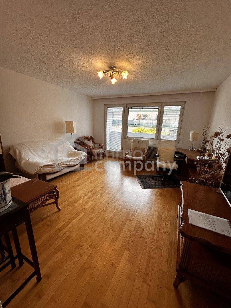 Gemütliches Wohnzimmer mit Parkettboden, Sofa und Blick auf die umliegenden Gebäude und Grünflächen.