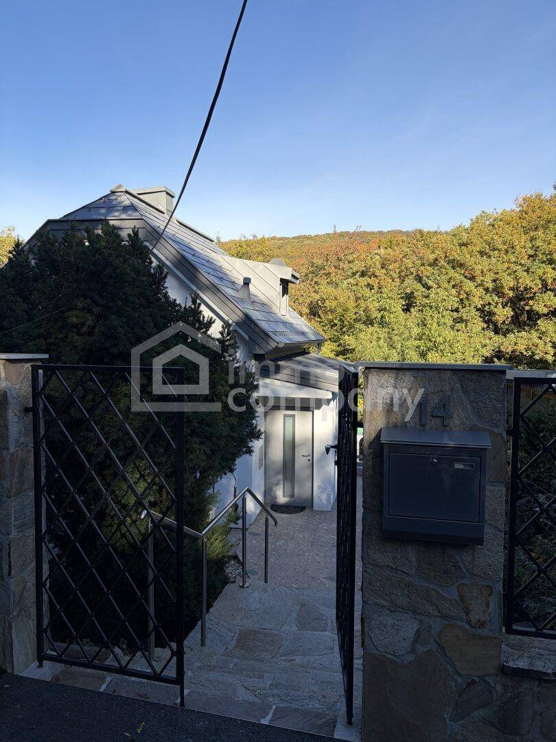 Eingangsbereich des Hauses mit Steintreppe, schmiedeeisernem Tor und umgebender Natur.