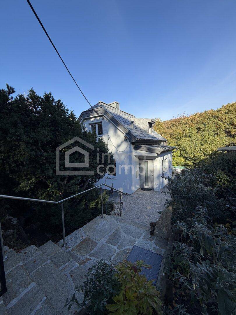 Steintreppe führt zum Haus, umgeben von üppigem Grün und herbstlicher Vegetation.