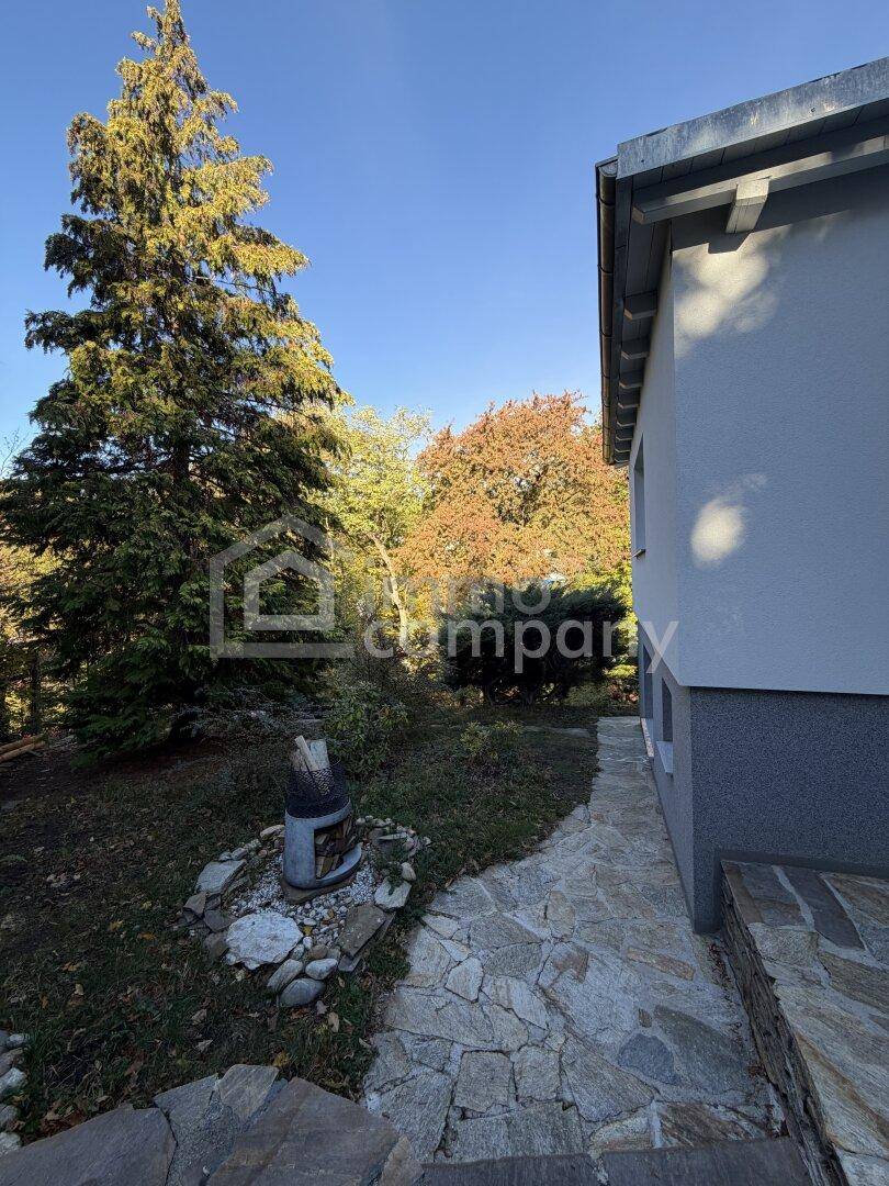 Steinweg entlang des Hauses führt in den Garten mit hohen Bäumen und Herbstfarben.