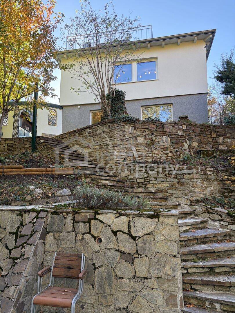 Terrassierte Gartenanlage mit Steinmauern und Treppen, die zum modernen Haus führen.