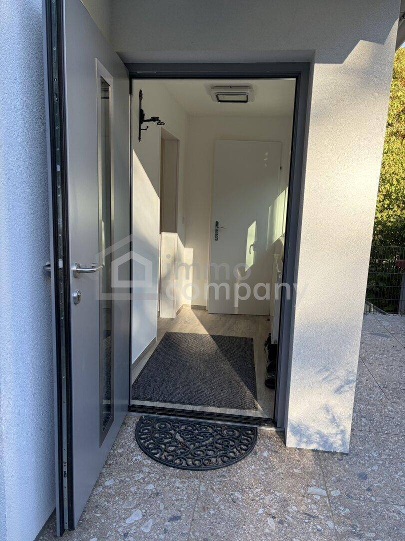 Heller Eingangsbereich mit offener Tür, Fußmatte und Blick in den Flur.