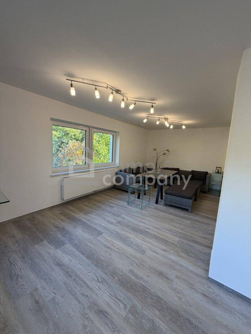 Helles Wohnzimmer mit Laminatboden, großen Fenstern und Blick ins Grüne.