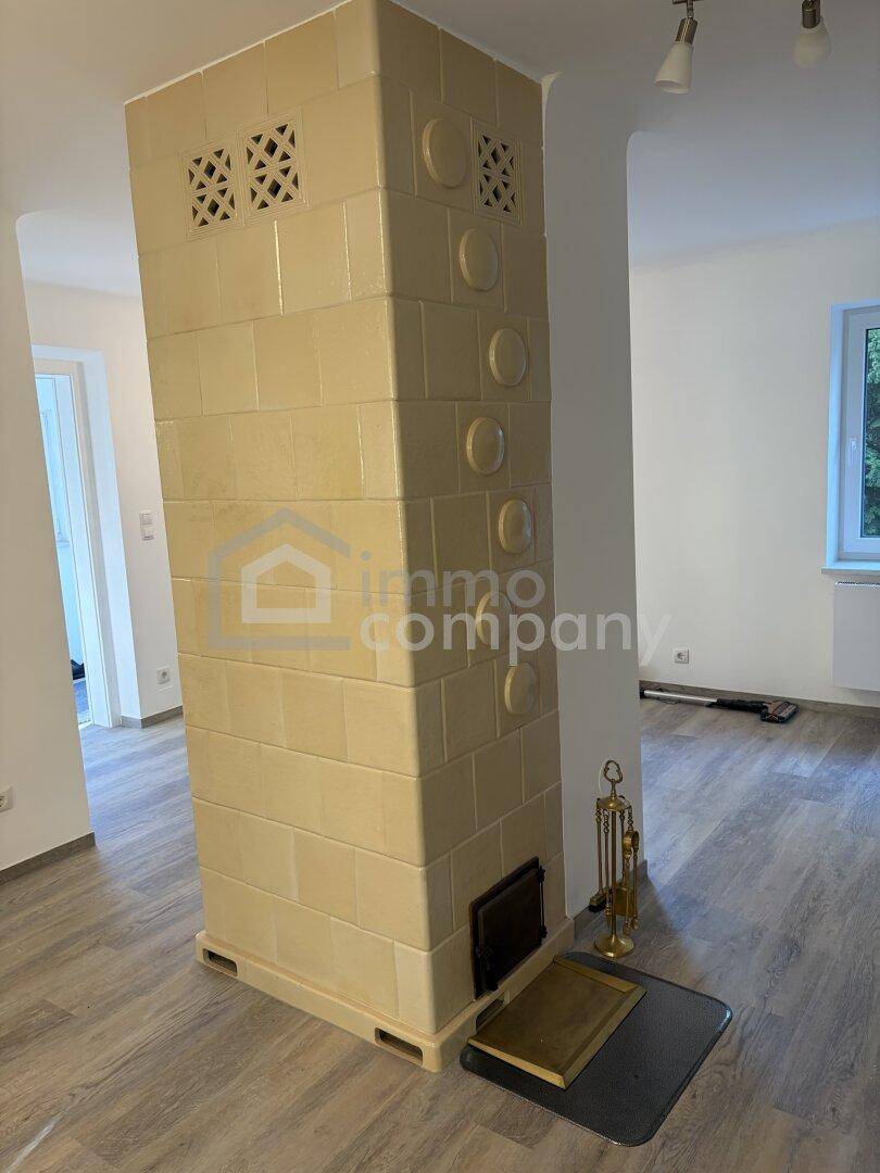 Traditioneller Kachelofen als zentrales Element im offenen Wohnbereich mit Laminatboden.
