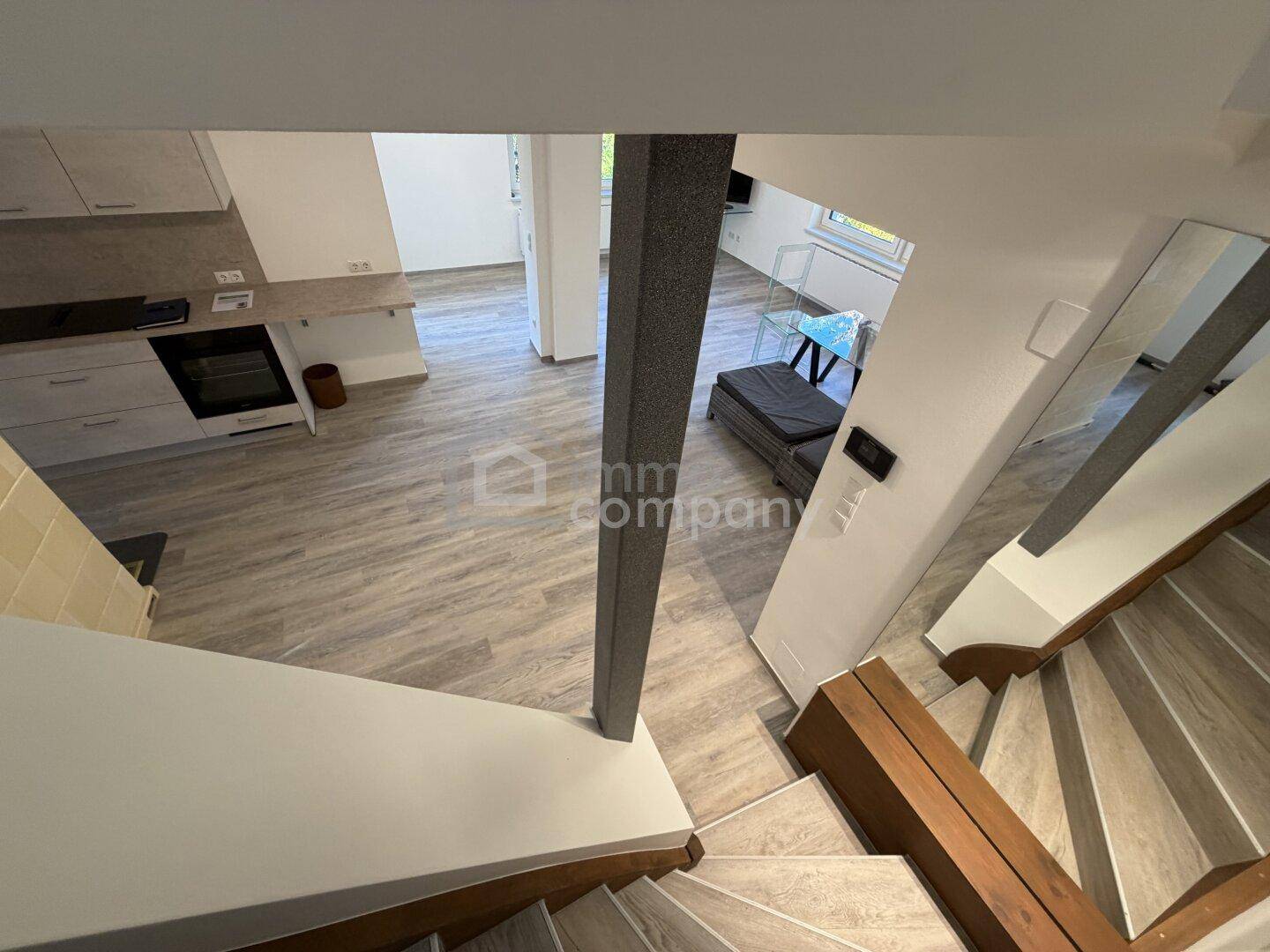 Blick vom Treppenabsatz auf den offenen Wohnbereich mit Küche und Laminatboden.