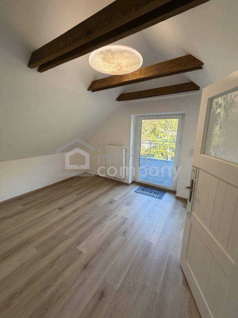 Helles Schlafzimmer im Dachgeschoss mit Holzbalken, Laminatboden und Zugang zum Balkon.
