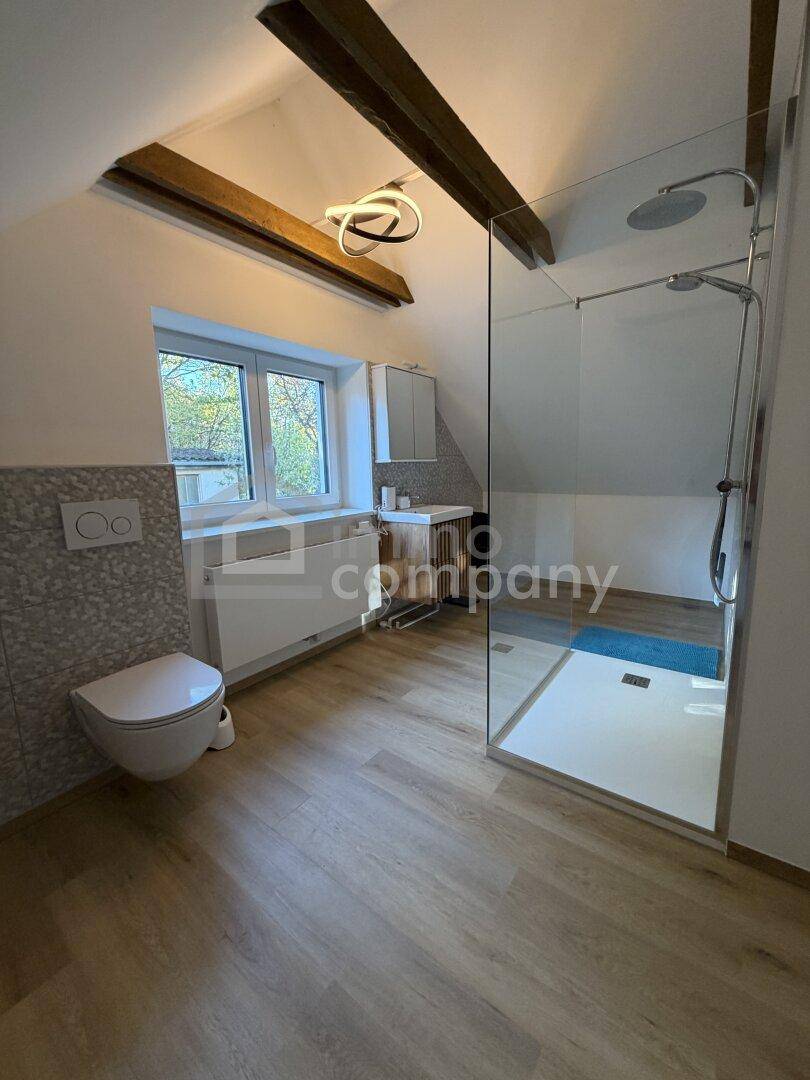 Modernes Badezimmer im Dachgeschoss mit begehbarer Dusche, Hänge-WC und Holzbalken.