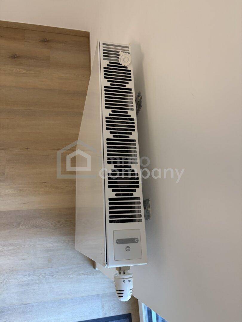 Nahaufnahme eines modernen Heizkörpers an einer weißen Wand mit Laminatboden.