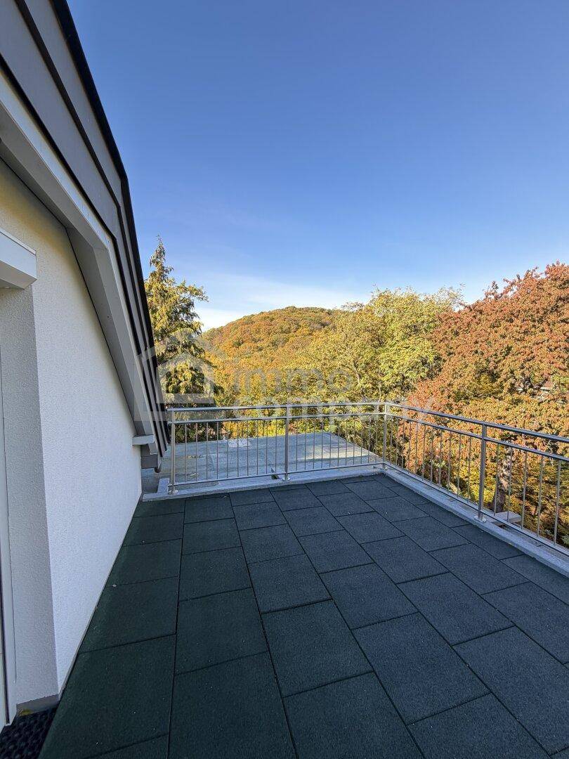 Geräumiger Balkon mit Fliesenboden und weitem Blick auf die bewaldete Hügellandschaft.