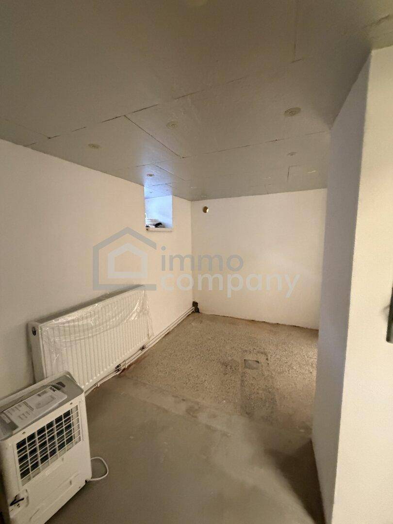 Kellerraum mit weiß gestrichenen Wänden, Heizkörper und kleinem Fenster.