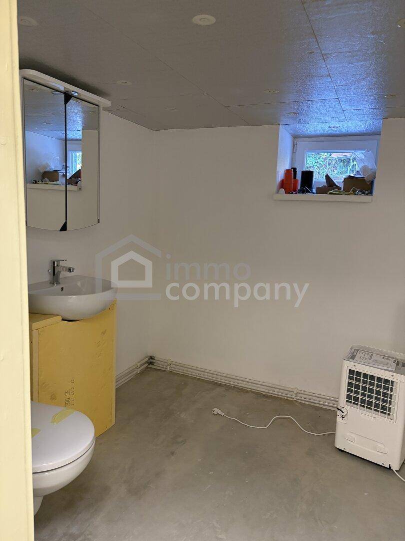 Einfaches WC im Keller mit Waschbecken, Spiegel und kleinem Fenster.