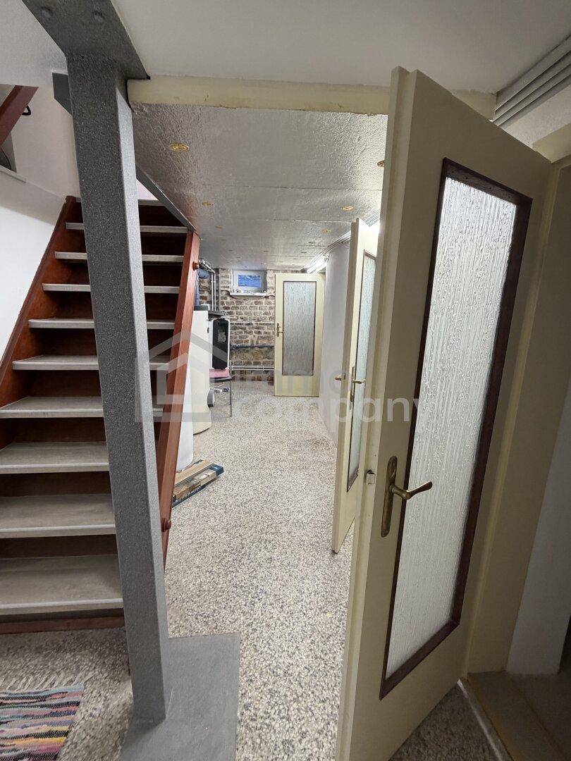 Kellerbereich mit Holztreppe, Stützpfeiler und Zugang zu weiteren Räumen.