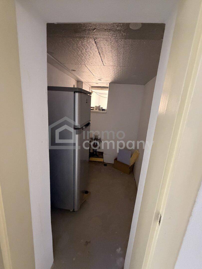 Schmaler Kellergang mit einem Kühlschrank und einfacher Ausstattung.