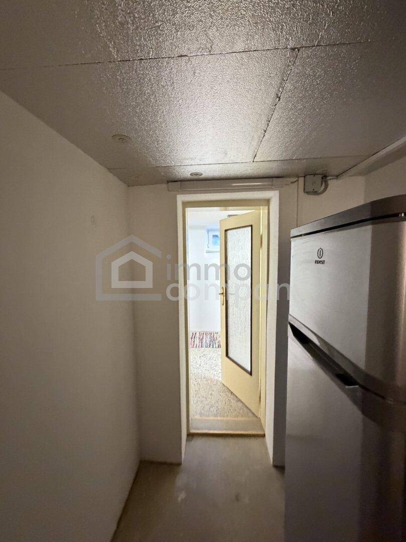 Kellerbereich mit Kühlschrank und Tür zu einem angrenzenden Raum.