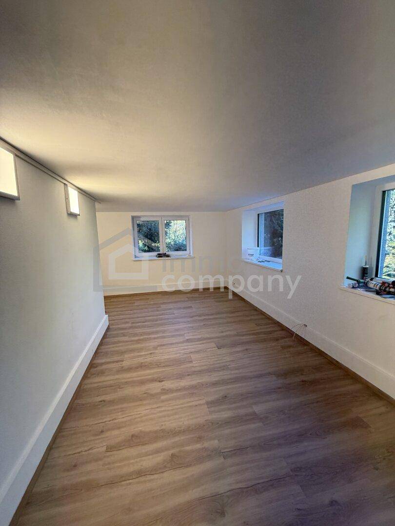 Renovierter Kellerraum mit Laminatboden und Fenstern, die Tageslicht hereinlassen.