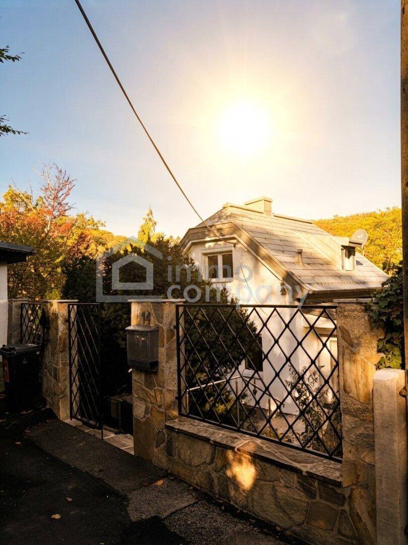 Sonniger Blick auf das Wohnhaus mit Steinfassade und schmiedeeisernem Tor im Herbstlaub.