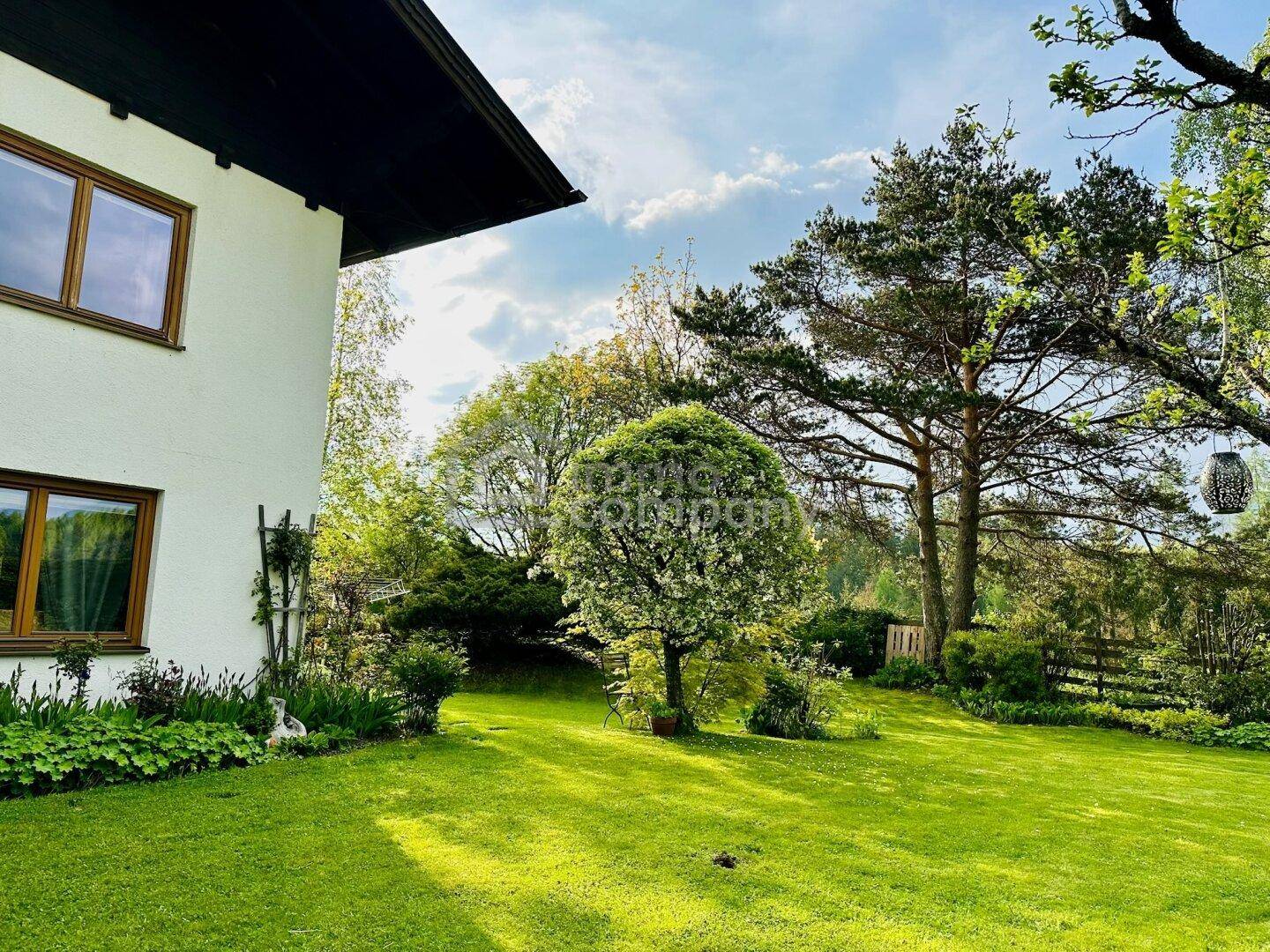 Weitläufiger, sonniger Gartenbereich mit Rasenfläche, Bäumen und Blick auf die grüne Umgebung.