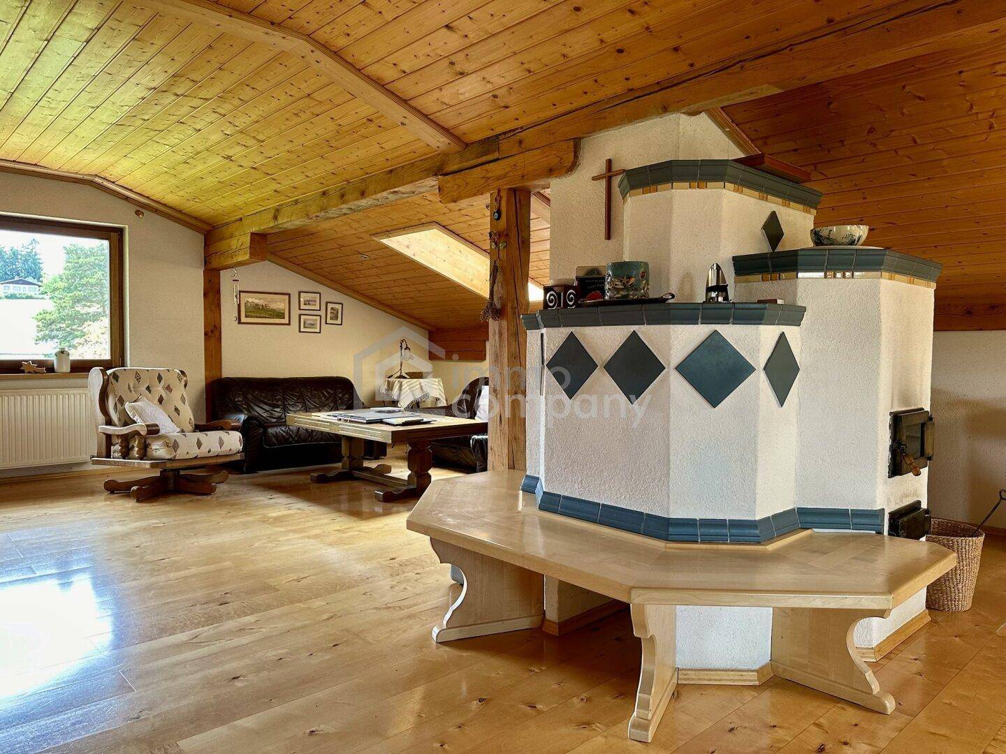 Rustikales Wohnzimmer mit Holzboden, Holzbalkendecke und einem traditionellen Kachelofen.