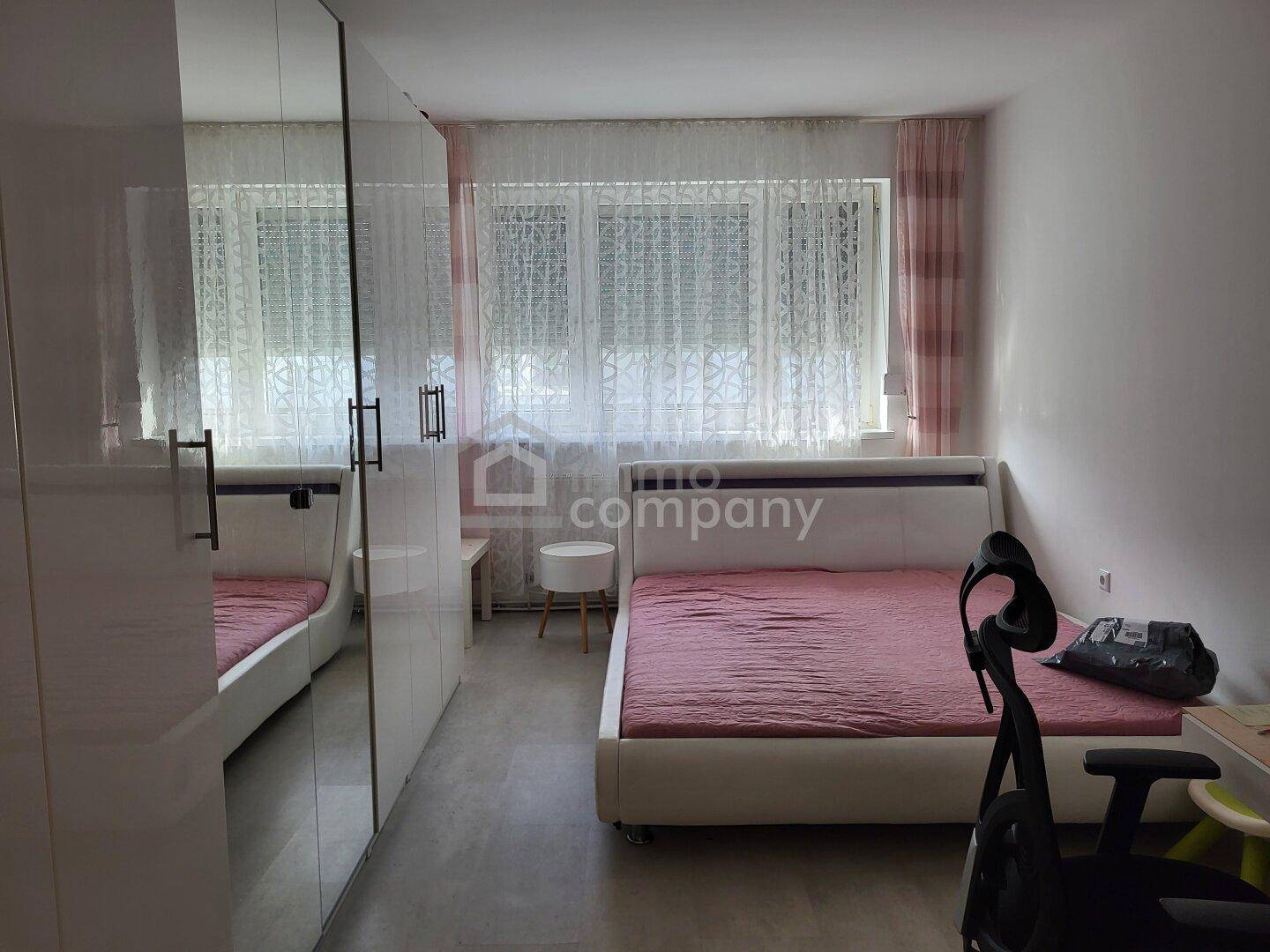 Helles Schlafzimmer mit Einzelbett, großem Kleiderschrank und Fenster mit Vorhängen.
