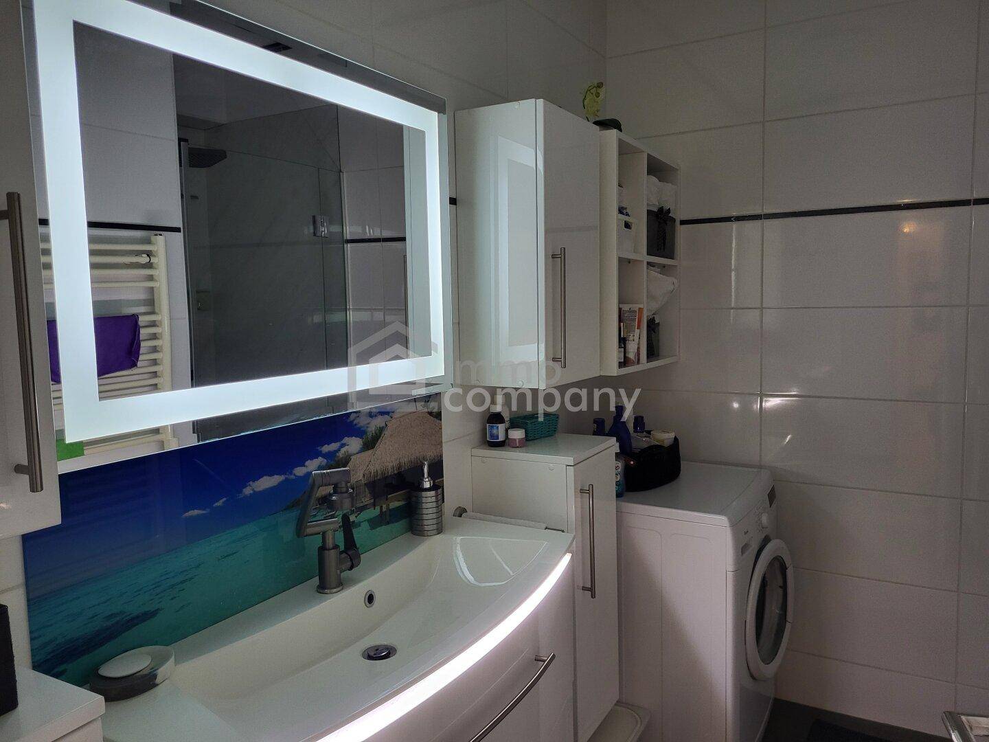 Modernes Badezimmer mit Waschbecken, beleuchtetem Spiegelschrank und Handtuchheizkörper.