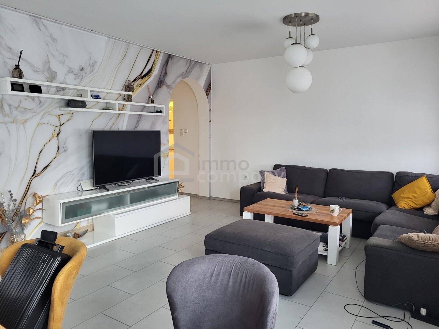 Gemütliches Wohnzimmer mit großem Ecksofa, Fernseher und dekorativer Wandgestaltung.