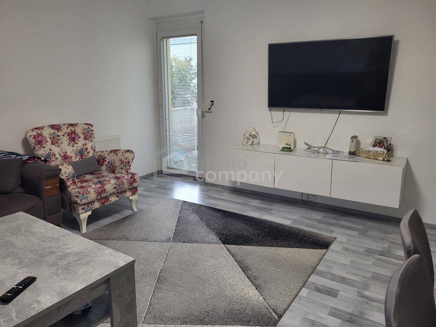 Gemütlicher Wohnbereich mit Wandfernseher, modernem Sideboard und Zugang zu einem Außenbereich.