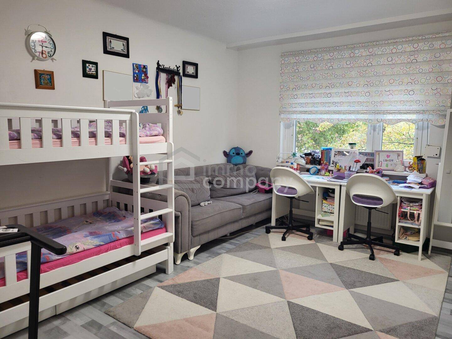 Kinderzimmer mit Etagenbett, Schreibtischen und einem gemütlichen Sofa, ideal für Spiel und Lernen.