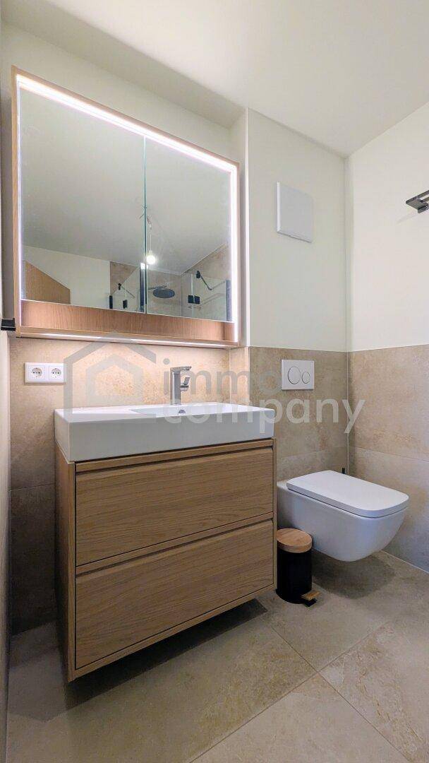 Modernes Badezimmer mit Holzwaschtisch, beleuchtetem Spiegelschrank und wandhängendem WC.
