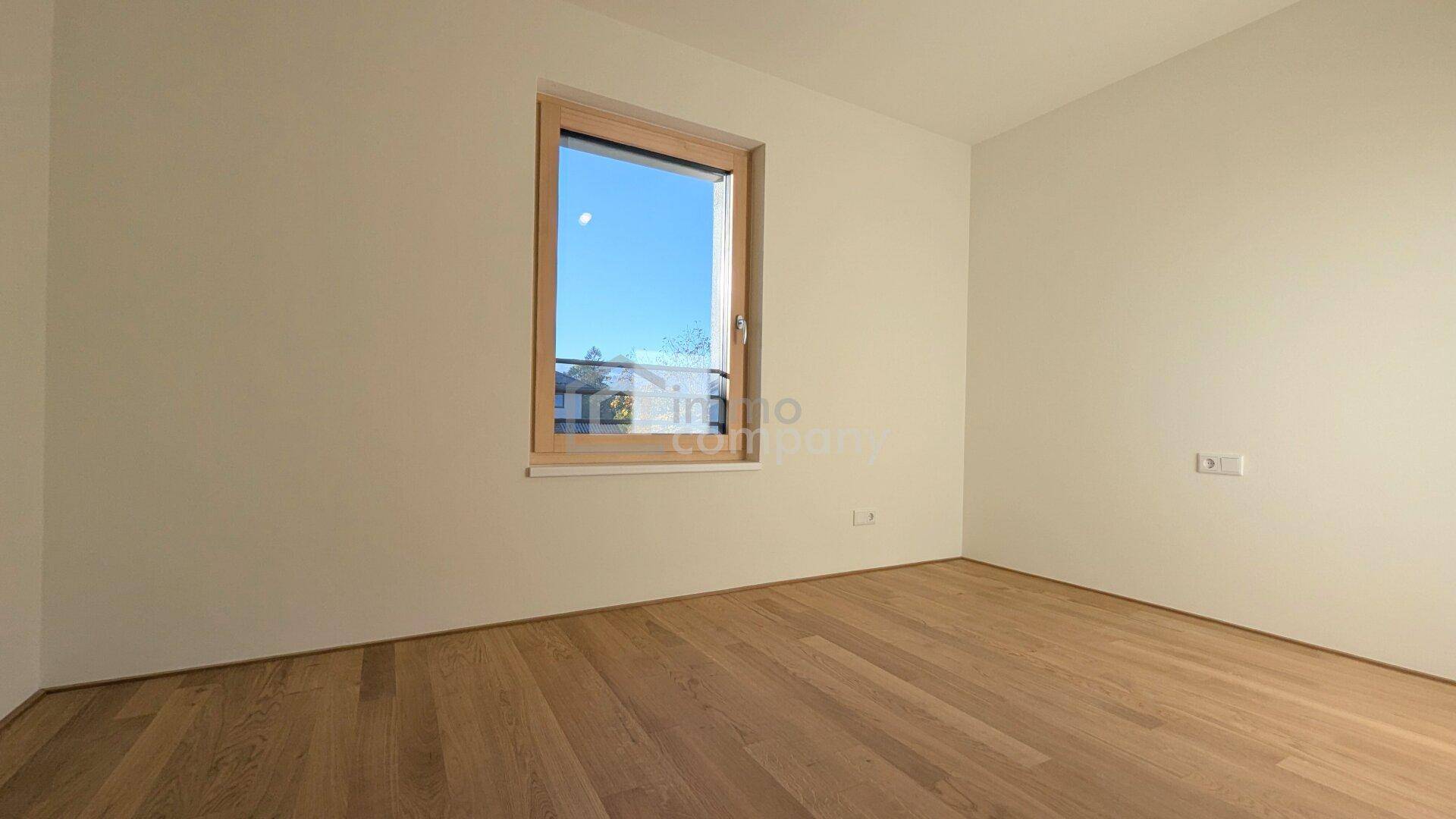 Leeres Zimmer mit Holzboden und einem großen Fenster, ideal als Büro oder Gästezimmer nutzbar.