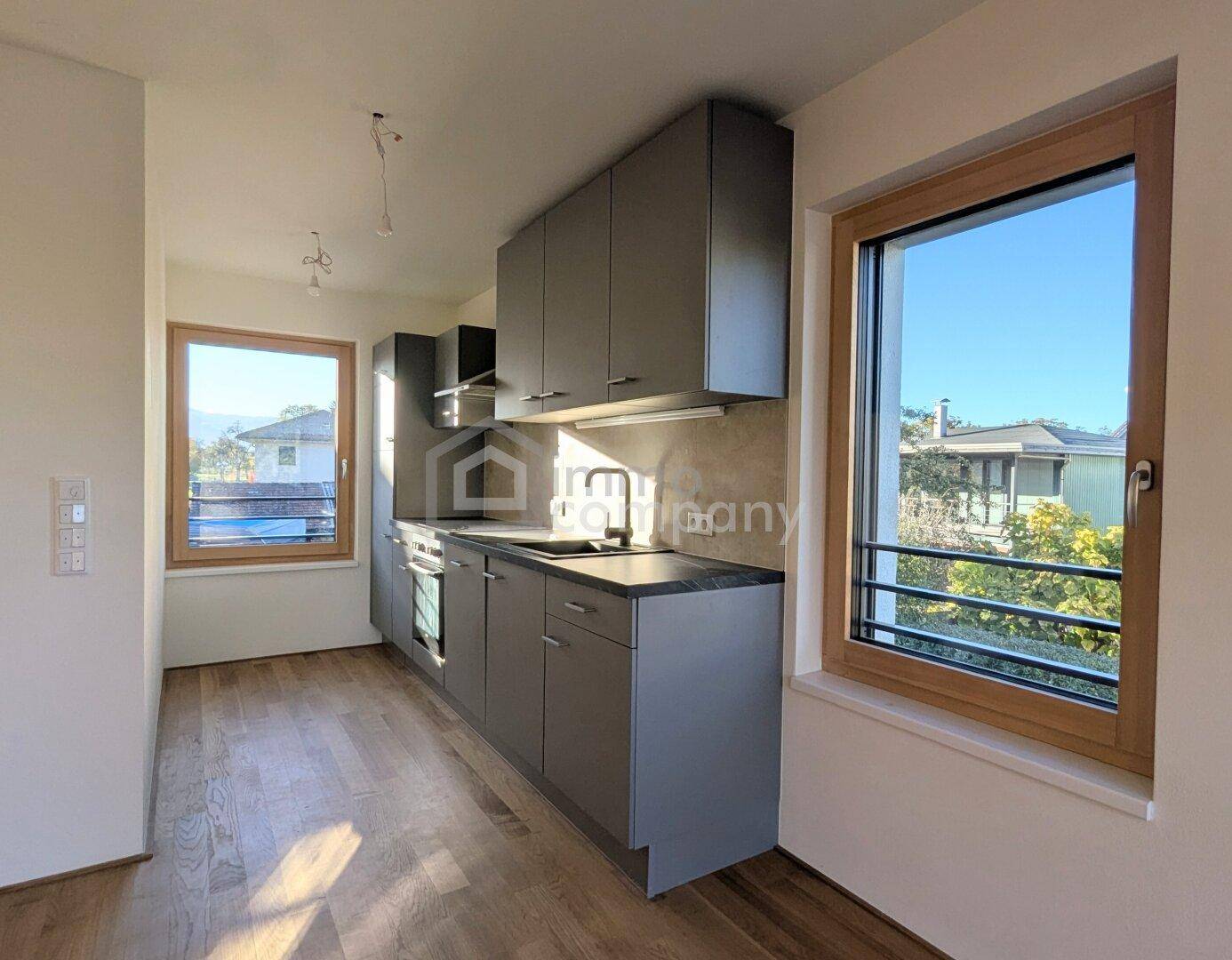 Moderne Küchenzeile mit grauen Schränken, integriertem Backofen und viel Tageslicht durch Fenster.