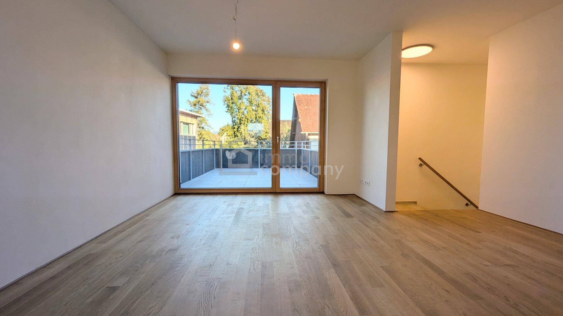 Lichtdurchfluteter Wohnbereich mit Holzboden und großer Schiebetür, die auf eine Terrasse führt.