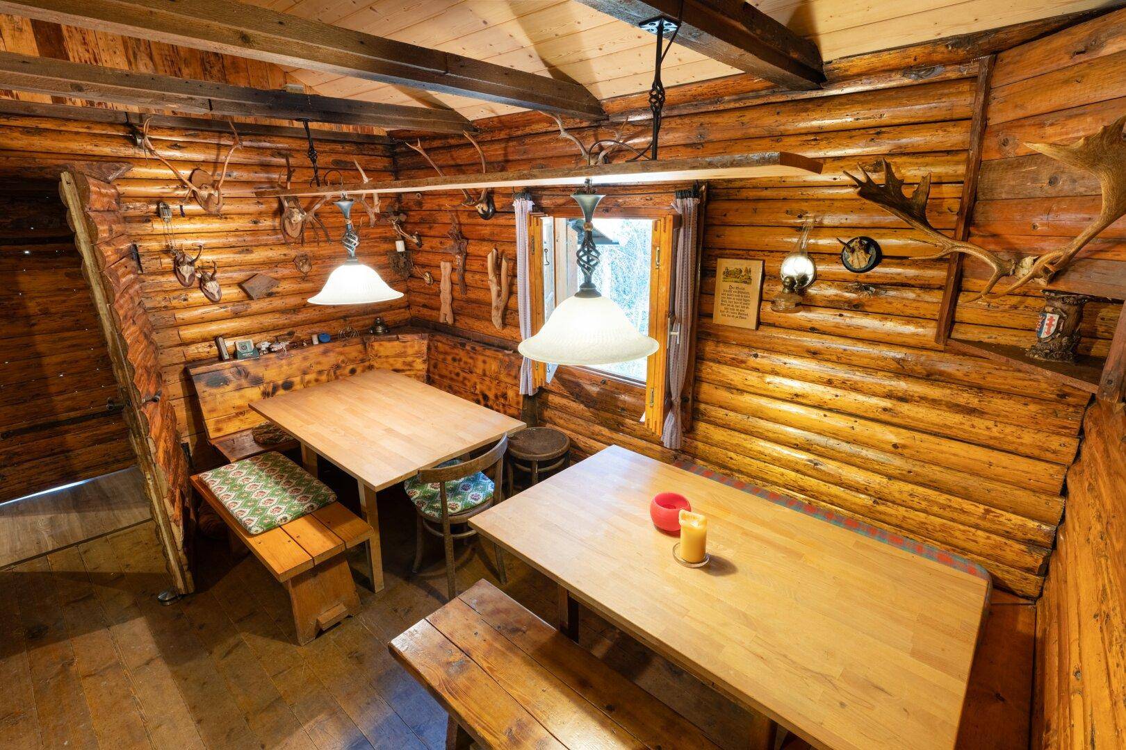 Gemütlicher Essbereich mit massiven Holztischen und Bänken, umgeben von rustikalen Holzstämmen.