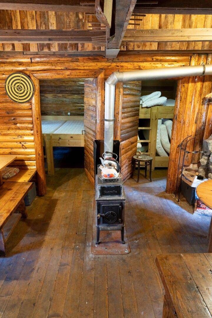Rustikaler Innenraum mit einem Holzofen als Mittelpunkt und Schlafbereichen im Hintergrund.